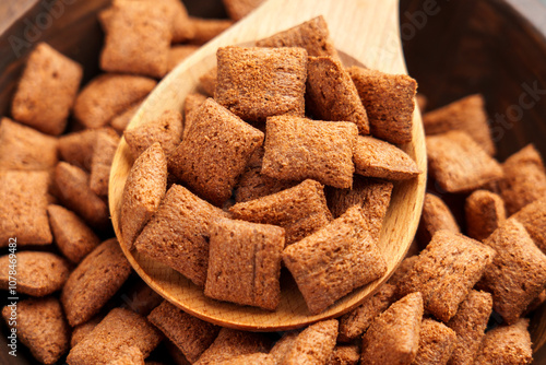 Brown corn cereal pillows with a rich chocolate crust in wooden spoon, capturing their crispy crunchy texture as a perfect breakfast. Top view photo