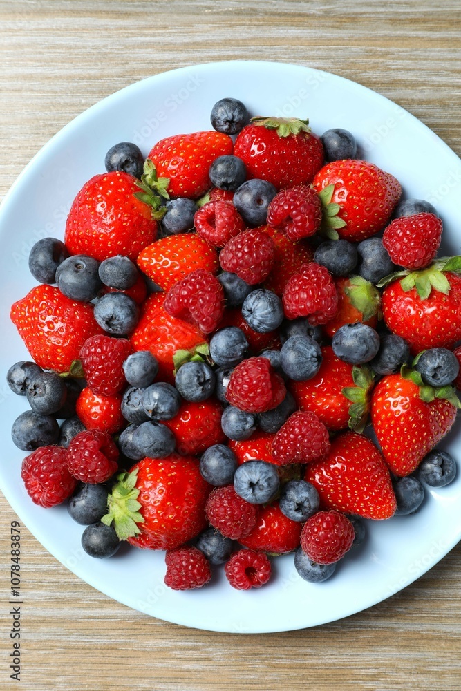 Different fresh ripe berries in bowl on wooden table, top view Different fresh ripe berries in bowl on wooden table, top view