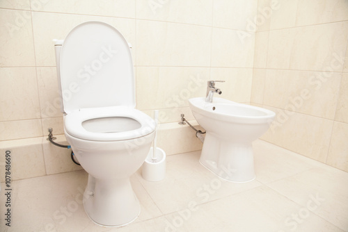 White Bidet and Toilet screwed in Bathroom,in Restroom, close-up. Beige Ceramic Floor Tiles. White bidet with chrome mixer