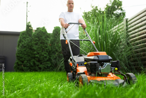 Obraz na plátně Gardener mowing grass with lawn mower in backyard garden