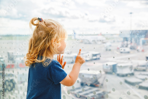 Cute little toddler girl at the airport, traveling. Happy healthy child waiting near window and watching airplanes. Family going on summer vacations by plane.