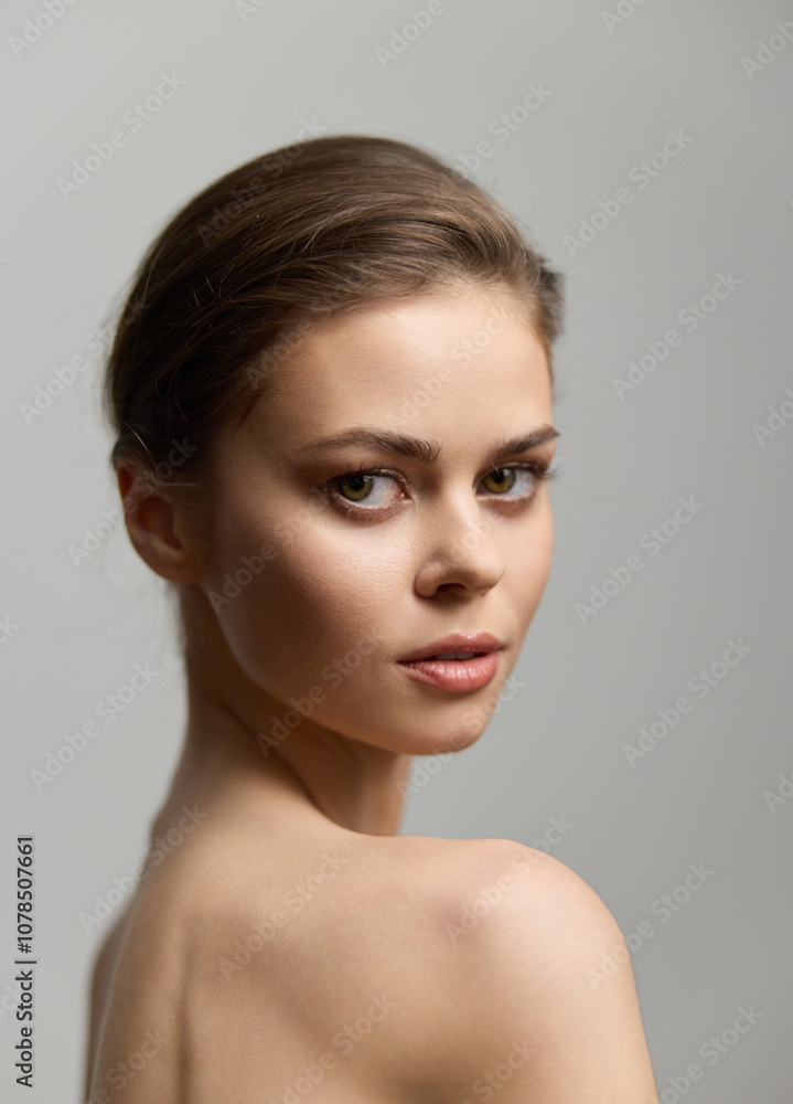 Beautiful young woman with an elegant hairstyle, gazing over her shoulder with a soft expression, showcasing natural beauty against a neutral background. Beautiful young woman with an elegant hairstyle, gazing over her shoulder with a soft expression, showcasing natural beauty against a neutral background.