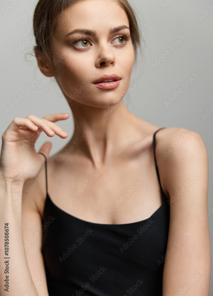 Thoughtful young woman with elegant features, gently touching her neck, wearing a simple black tank top, showcasing beauty and contemplation. Thoughtful young woman with elegant features, gently touching her neck, wearing a simple black tank top, showcasing beauty and contemplation.