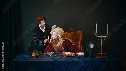 Royal empress in baroque gown, holding cigarette as her loyal favorite standing beside with candle against dark vintage background. Elderly woman with young man. Concept of history, comparison of eras