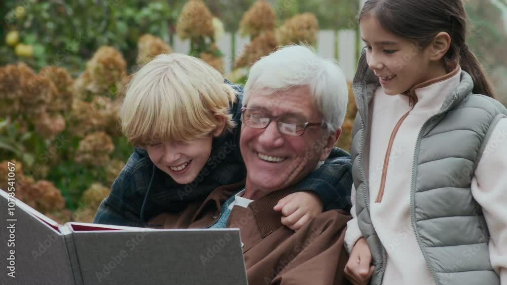 Loving grandparent sharing joyful storytime with his grandchildren, huddled together with book in beautiful outdoor setting of lush garden with blooming fall flowers Loving grandparent sharing joyful storytime with his grandchildren, huddled together with book in beautiful outdoor setting of lush garden with blooming fall flowers