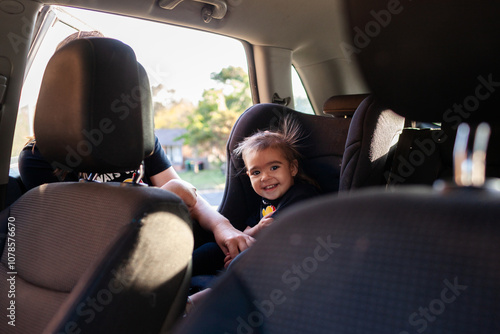 Australian mum putting Aboriginal toddler girl into forward facing car seat ready to travel photo