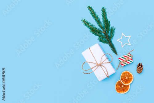 Collection of Christmas objects - goft box, eve fir, dried orange, pine cone, wooden star on light blue background. New Year and winter minimal holiday frame composition. Flat lay, top view photo