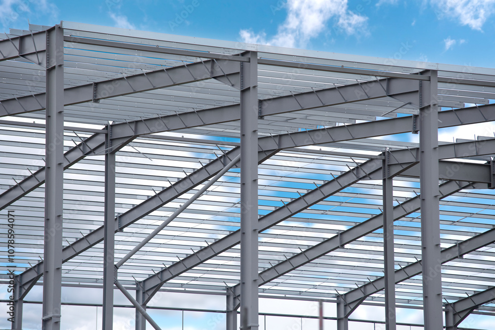 Construction of a steel structure against a blue sky with clouds at a building site during daytime Construction of a steel structure against a blue sky with clouds at a building site during daytime