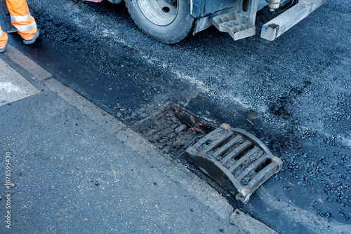 Construction worker operates a vacuum truck to clear debris from a storm drain on a busy city street photo