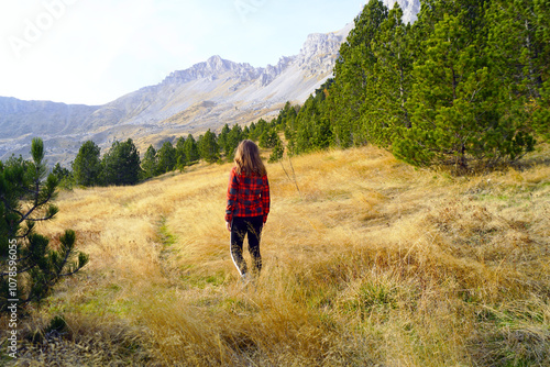 Walking on the circular route in Komovi Nature Park, Montenegro: photographed from behind, a female tourist stands on a forest clearing with yellow grass and looks at the scenic mountain view. photo