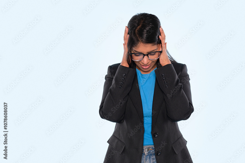 Young woman in a black blazer experiencing stress while standing in a light blue background Young woman in a black blazer experiencing stress while standing in a light blue background