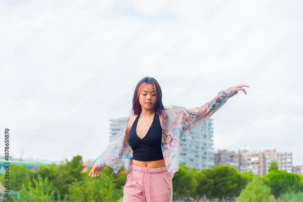 Young Asian woman dancing outdoors amidst urban greenery Young Asian woman dancing outdoors amidst urban greenery