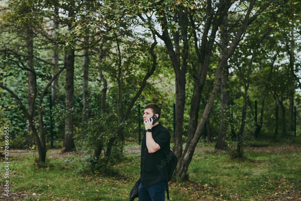 Portrait of confident Caucasian man in black casual talking on phone in autumn park Portrait of confident Caucasian man in black casual talking on phone in autumn park