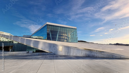 Fotografía Oslo Opera House under a clear blue sky, featuring sleek glass facades and minimalist Scandinavian design, a striking symbol of modern architecture and Norwegian culture
