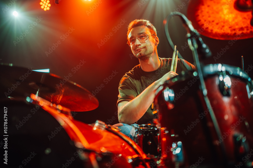 Fototapeta premium Drummer playing drums on stage with warm lighting