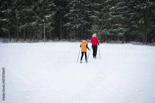 Happy family winter fun - child and grandmother skiing at snowy forest, rear view