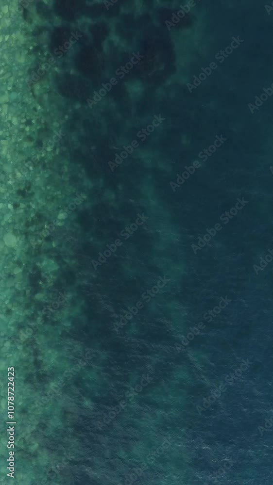 Aerial vertical view of beach with wave caressing shore. Sun glare, small waves on the water surface. Sunset. Evening. Nobody. No people. Summer travel and vacation.