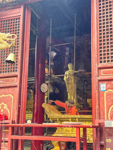 Denfeng, China - October 28, 2024 A artisan restores a Buddhist temple adorned with a gleaming golden statue and intricate designs, coloring buddha in Shaolin temple. photo