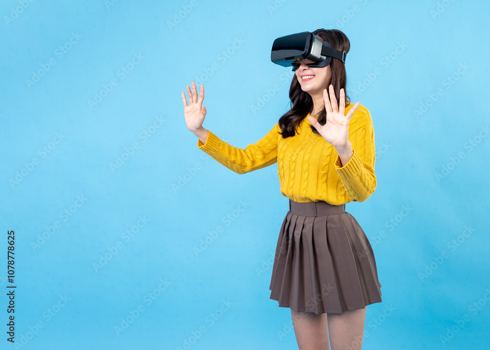 Excited young woman in VR headset touching air during virtual reality experience at studio. Emotional lady exploring artificial computer world or playing video game isolated on light blue background Excited young woman in VR headset touching air during virtual reality experience at studio. Emotional lady exploring artificial computer world or playing video game isolated on light blue background