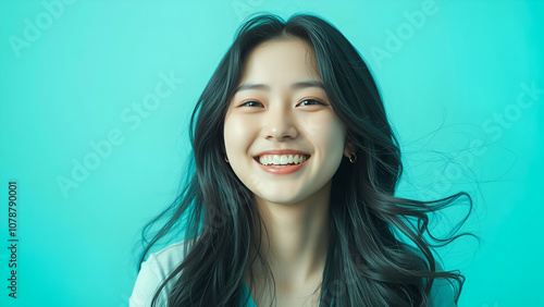 Joyful young korean woman with long black hair smiles brightly against vibrant turquoise background