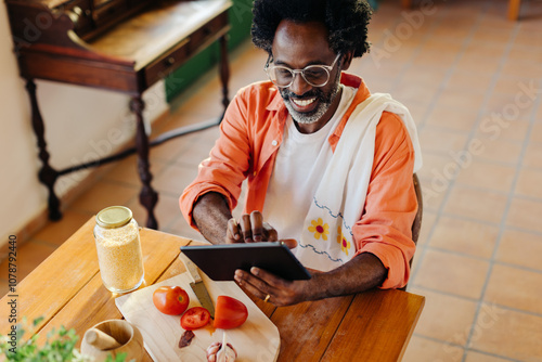 Canvas-taulu Cheerful man making traditional Brazilian cuisine at home using a digital tablet