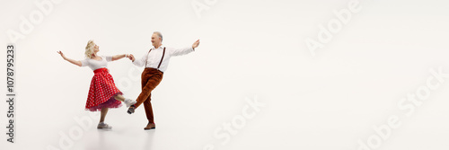 Senior couple, stylish man in suspenders and elegant woman in polka dot dress, dynamically dancing isolated on white background. Concept of retro dance, hobby, aging, active lifestyle photo