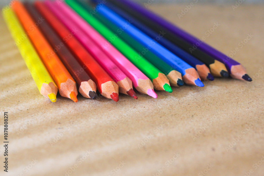 Colored pencils neatly arranged in a row, displaying a vibrant spectrum of colors on a brown surface. Perfect for themes related to art, education, and creativity. Colored pencils neatly arranged in a row, displaying a vibrant spectrum of colors on a brown surface. Perfect for themes related to art, education, and creativity.