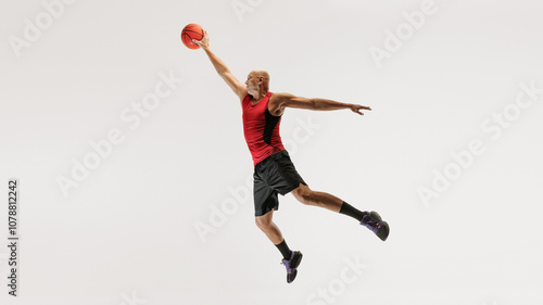 Wallpaper Mural Young man in athletic clothing, wearing tank top and shorts, jumps with basketball toward hoop against grey studio background. Concept of sport event, competition, active and healthy lifestyle, game. Torontodigital.ca