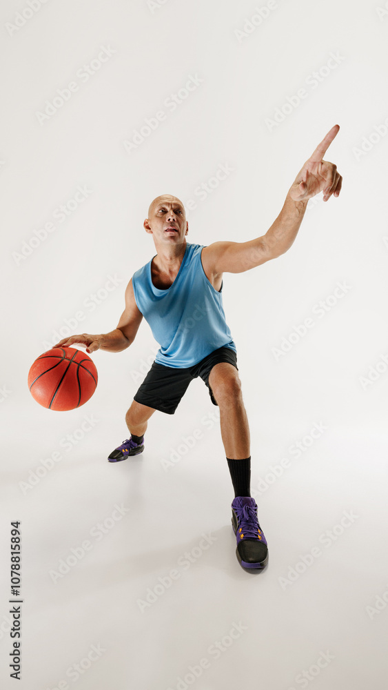 Man dressed in athletic gear dribbles basketball, ready to make move against grey studio background. Wide angle. Concept of sport event, competition, active and healthy lifestyle, game. Man dressed in athletic gear dribbles basketball, ready to make move against grey studio background. Wide angle. Concept of sport event, competition, active and healthy lifestyle, game.