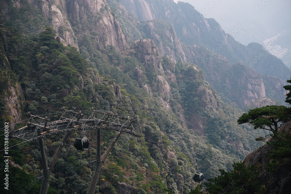 Naklejka premium Cable car through the mountains to arrive at the Yellow Mountain in Huangshan, China, with view of the city in the background on a foggy day of autumn