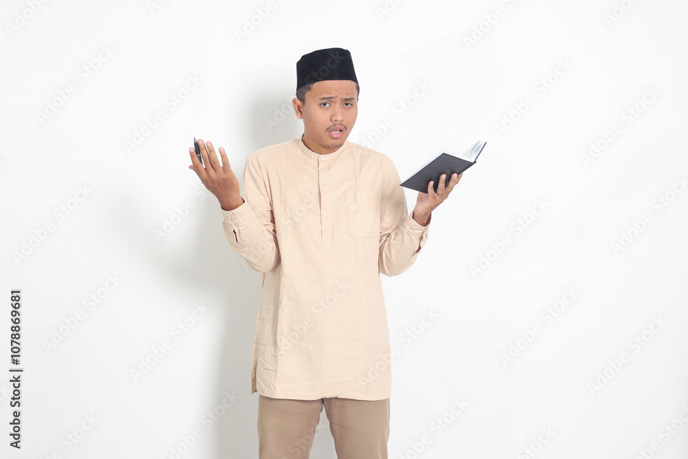 Portrait of confused Asian muslim man in koko shirt with peci difficulty understanding the contents of the book, reading a textbook. Isolated image on white background Portrait of confused Asian muslim man in koko shirt with peci difficulty understanding the contents of the book, reading a textbook. Isolated image on white background