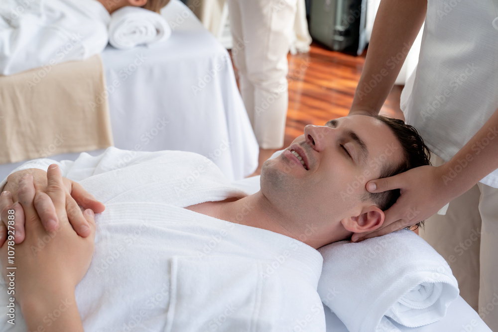 Caucasian couple enjoying relaxing anti-stress head massage and pampering facial beauty skin recreation leisure in dayspa modern light ambient at luxury resort or hotel spa salon. Quiescent Caucasian couple enjoying relaxing anti-stress head massage and pampering facial beauty skin recreation leisure in dayspa modern light ambient at luxury resort or hotel spa salon. Quiescent