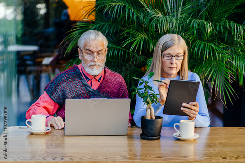 Elderly couple working together on laptop and tablet in cafe photo