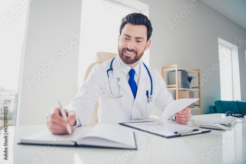 Photo of experienced doctor guy sit table hold paper check list write copybook in hospital room