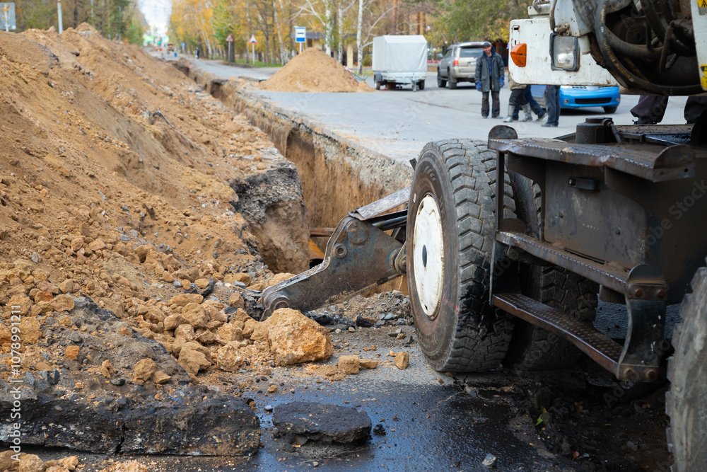 An excavator next to a deep long earthen trench for laying a large diameter water pipe. construction work to replace a city water pipe An excavator next to a deep long earthen trench for laying a large diameter water pipe. construction work to replace a city water pipe