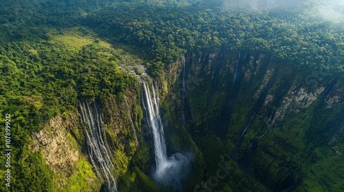 Aerial view of a large waterfall cascading down a steep cliff face surrounded by lush green forest.