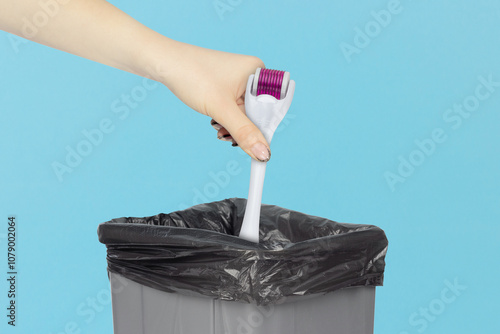 throw a Mesoscooter, mesoscooter Dermaroller. Device for cosmetic mesotherapy procedures into the trash bin, hold а mesoscooter in your hand in front of a trash can photo