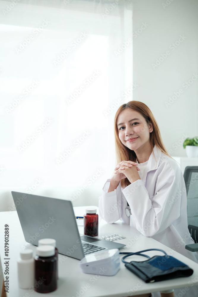 A woman in a white lab coat sits at a desk with a laptop and a bottle of pills A woman in a white lab coat sits at a desk with a laptop and a bottle of pills