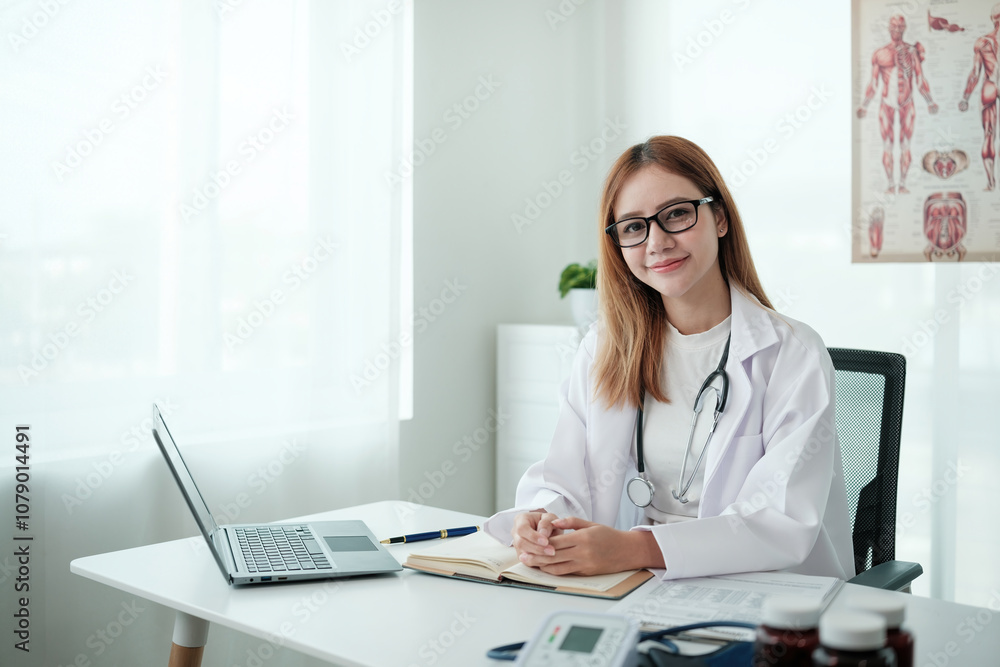 A woman in a white lab coat sits at a desk with a laptop and a book A woman in a white lab coat sits at a desk with a laptop and a book