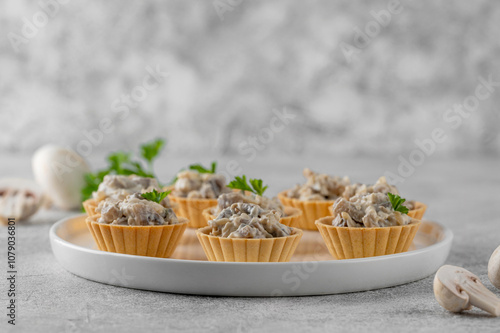 Canvastavla Mini tartlets with mushrooms in a cream sauce, with cheese, garlic and herbs on a white plate on a gray concrete background