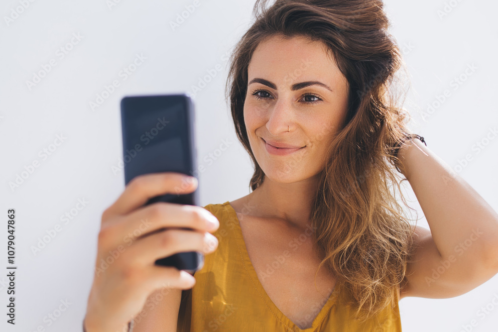 Smiling gorgeous lady in modern outfit capturing selfie photo by mobile on gray blank background Smiling gorgeous lady in modern outfit capturing selfie photo by mobile on gray blank background