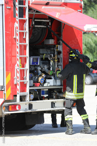 firefighter in a uniform wearing a protective helmet near a red fire truck is grabbing a hose to extinguish a fire photo