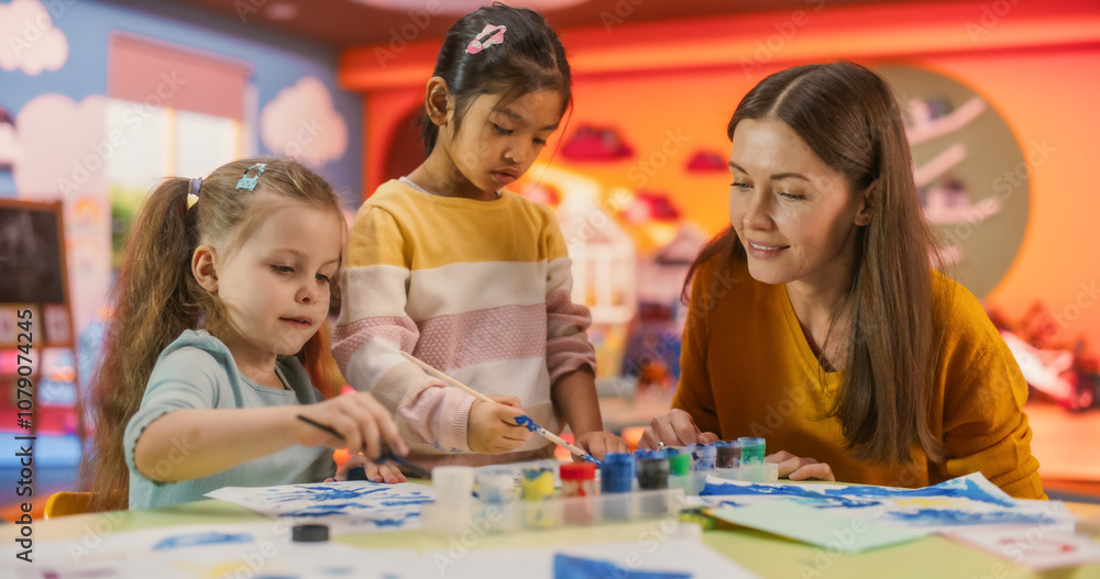 Fototapeta premium Portrait of Two Adorable Girls Using Watercolor to Create Colorful Paintings on Paper. Cheerful Female Teacher Spending Productive Time in Preschool, Teaching Kids to Paint in Art Class