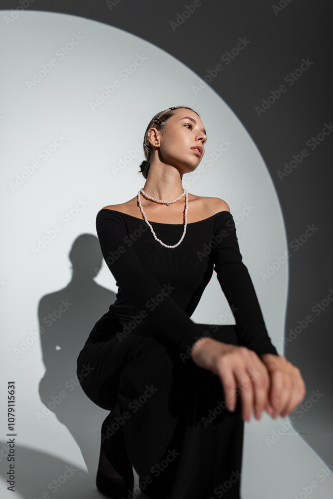 Glamorous beautiful young woman in fashionable black dress sitting and posing in studio on dark background. Lady at party Glamorous beautiful young woman in fashionable black dress sitting and posing in studio on dark background. Lady at party
