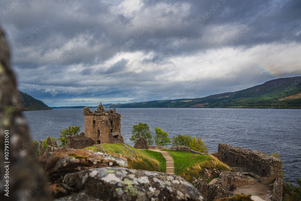 Ruins of Urquhart Castle in the Highlands of Scotland besides Loch Ness lake in background with dramatic sky and part of rainbow. Ruins of Urquhart Castle in the Highlands of Scotland besides Loch Ness lake in background with dramatic sky and part of rainbow.