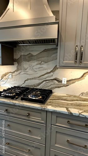 A modern kitchen with grey cabinets, a stainless steel range hood, and a marble countertop