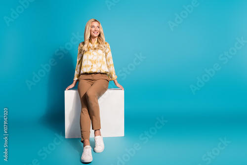 Full length photo of stunning mature lady sit cube look empty space dressed stylish formalwear clothes isolated on cyan color background photo