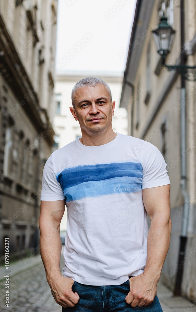 A man in a white shirt with blue stripes stands on a city street. He is smiling and looking at the camera A man in a white shirt with blue stripes stands on a city street. He is smiling and looking at the camera