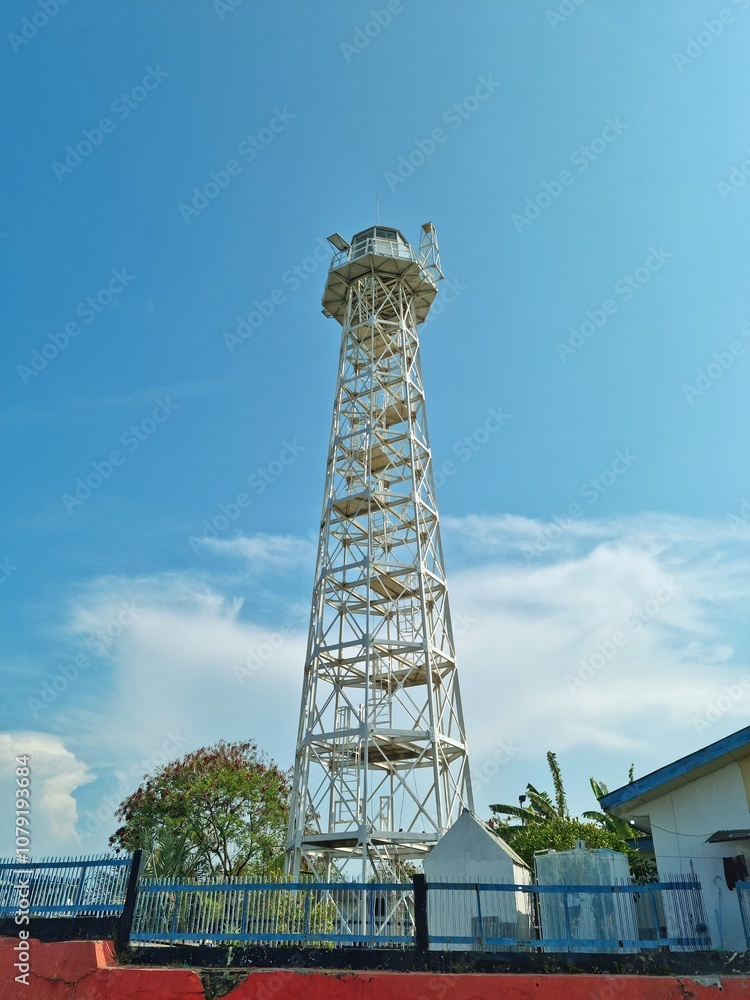 Cirebon, Indonesia - Nov 02, 2024: White lighthouse made of steel with greenery trees and grey sky as the background Cirebon, Indonesia - Nov 02, 2024: White lighthouse made of steel with greenery trees and grey sky as the background