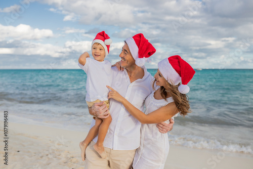 Happy family celebrates Christmas on the beach. Mom, dad and son in holiday hats on the beach celebrate the New Year